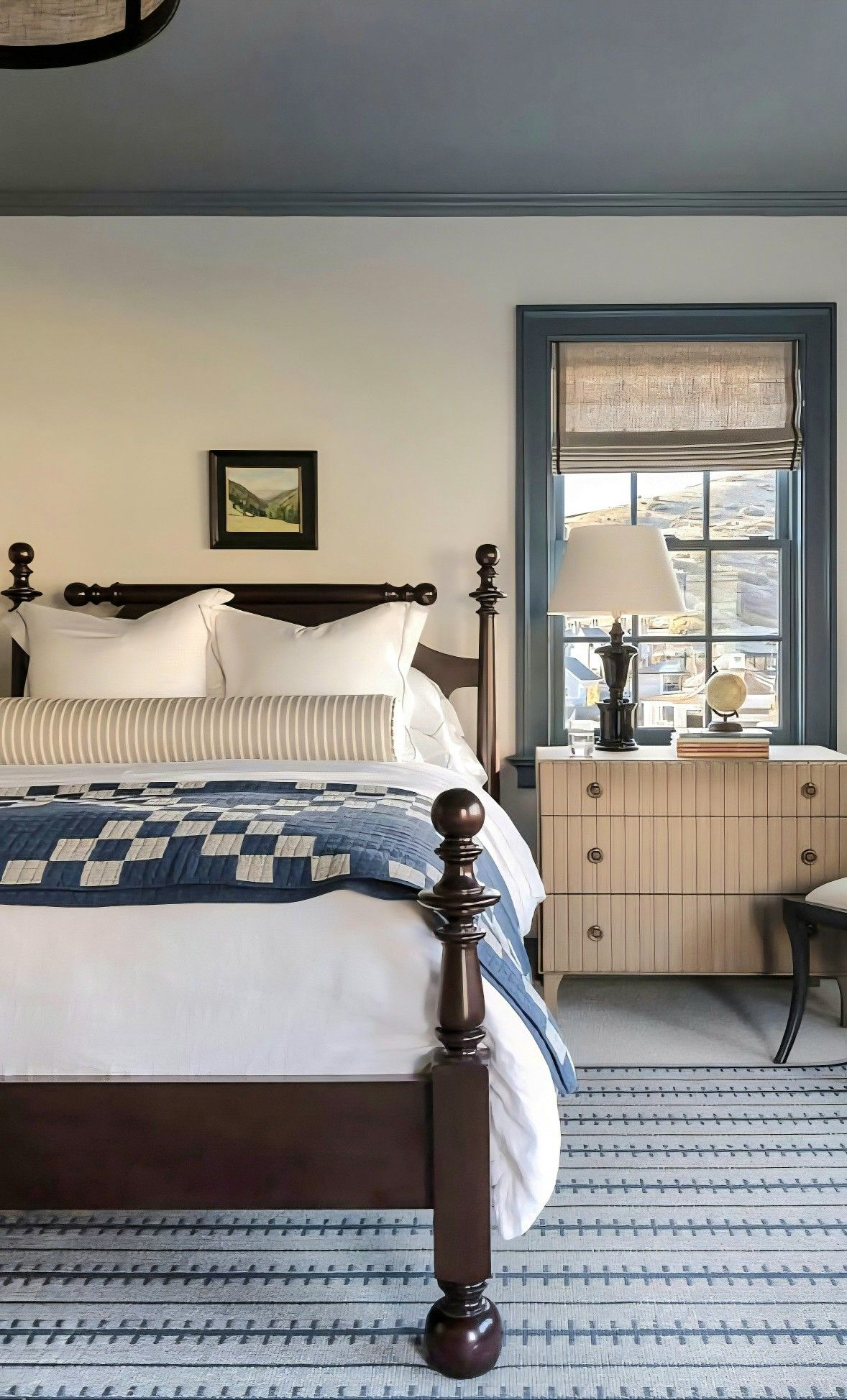 Classic bedroom with a dark wood four-poster bed, white linens, an indigo patchwork quilt, a slate-blue ceiling and a fluted wood dresser by the window
